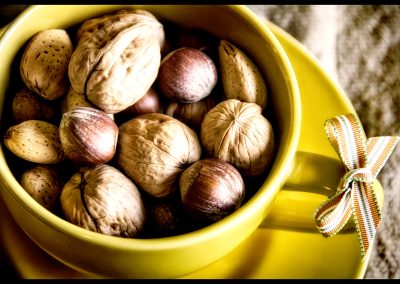 A close up photo of a yellow cup full of a variety of nuts. A small striped ribbon is tied to the handle of the cup.